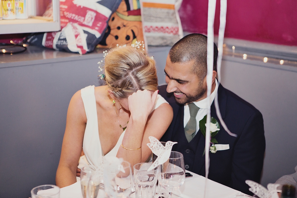 Bride and groom giggle together during wedding speeches London